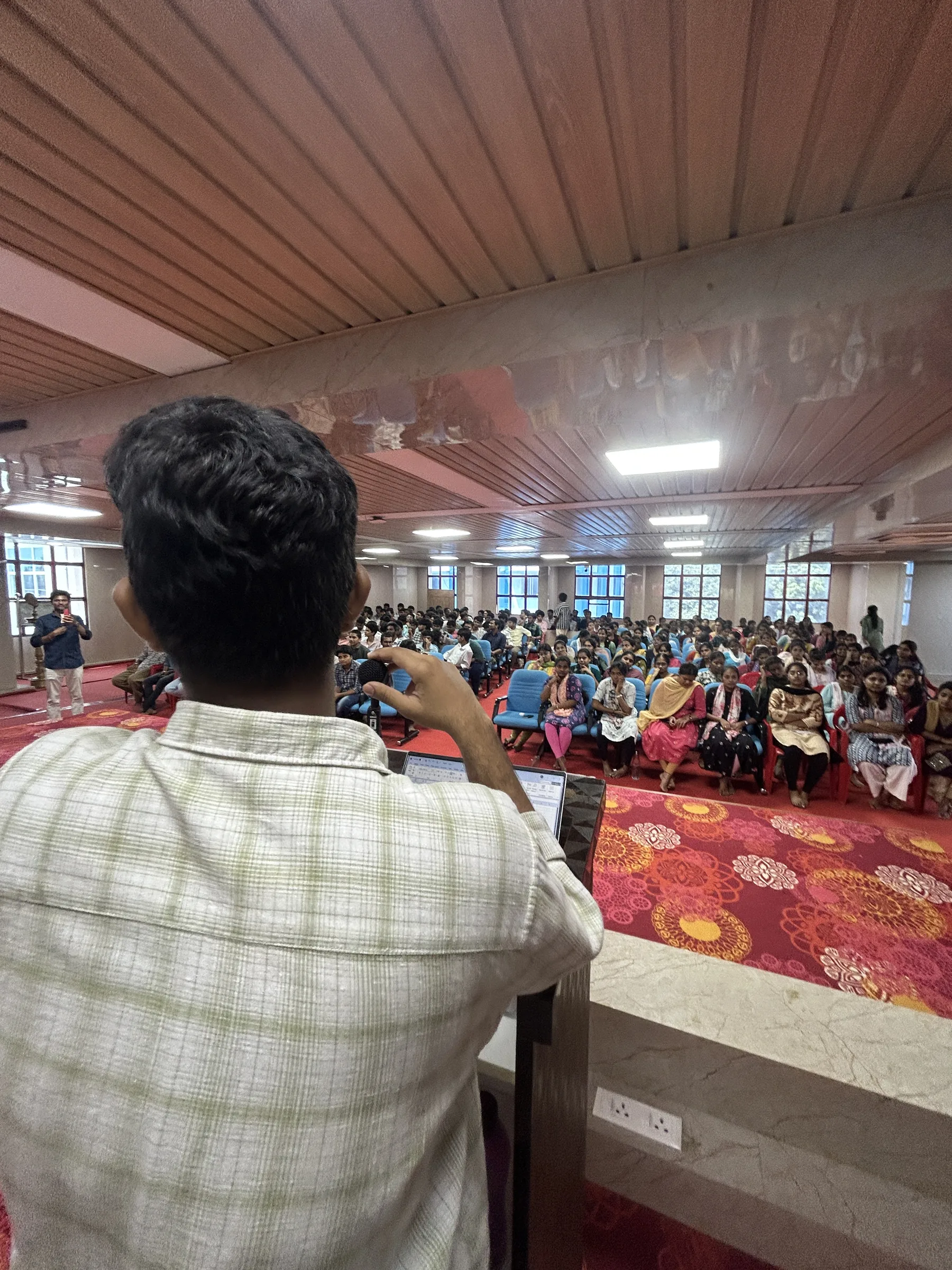 A student host speaking to the Freshie Intro audience from the front of the hall